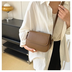 Brown vintage saddle bag worn by a model in a minimal interior, detail on smooth leather