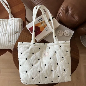 Detail of quilted off-white tote bag with black polka dots and French text patch