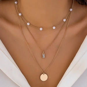 Detailed close-up of a three-layer gold necklace with faux pearls and geometric pendants