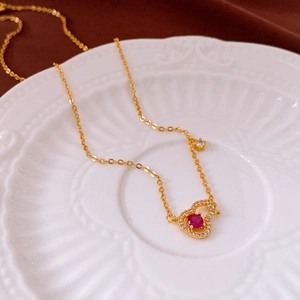 Detailed view of a gold-plated heart necklace with a red stone on a white ceramic plate