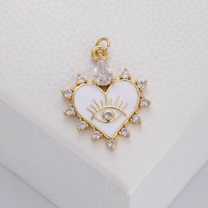 Macro view of a gold heart pendant with white enamel eye and clear zircon stones