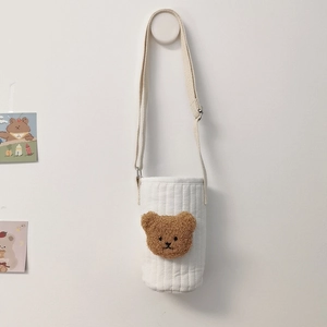 Close-up of quilted white cotton cup holder with brown plush bear head and beige strap