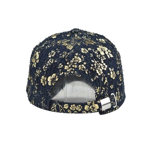 Detail of navy tweed baseball cap featuring gold floral print and silver metal buckle strap