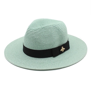 Close-up of mint green straw fedora hat featuring a black band with a gold bee ornament