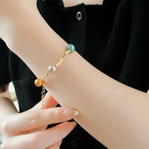 Detail of adjustable gold wavy bracelet with green, pink, and orange gold pearls
