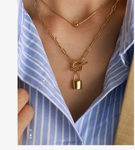 Detail of layered gold necklace with padlock pendant and toggle clasp on a model