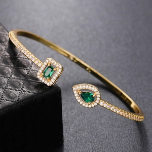 Macro shot of an open gold bangle with a green emerald stone and white zircon accents