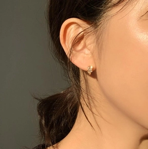 Close-up of elegant gold stud earrings with clear zircon on model under warm sunset light