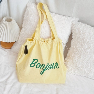 Detail of a yellow canvas tote bag with green Bonjour text in a cozy home setting