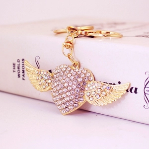 Golden heart wing keychain with colorful rhinestones resting on a book with pink background