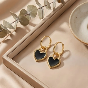 Detail of gold heart earrings with black enamel on a beige jewelry tray backdrop