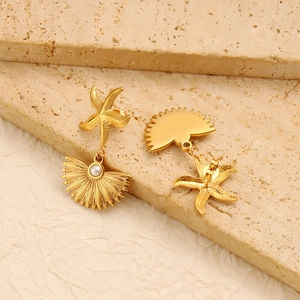 Detail of golden starfish and shell earrings with white pearls on a stone background