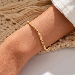 Nahaufnahme eines goldenen Kordelarmbands mit gedrehter Textur an einem Handgelenk
