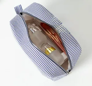 Macro shot of large capacity seersucker makeup bag with blue and white stripes and brushes
