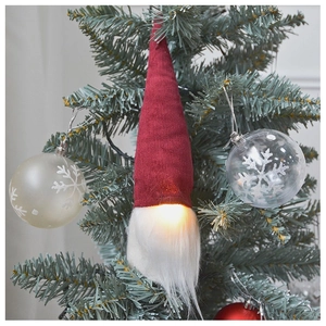 Close-up of a glowing Christmas gnome with red hat and white beard on a pine tree
