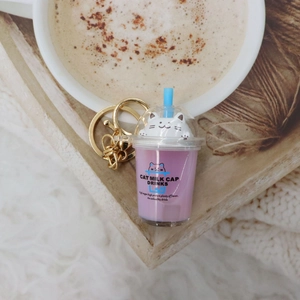 Detail of pink cat milk tea cup keychain with golden lobster clasp on a wooden tray