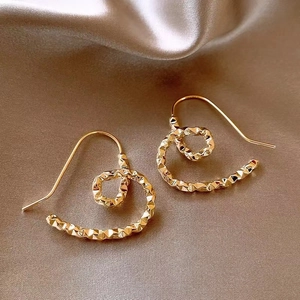 Macro shot of gold-plated twisted heart earrings on elegant champagne silk background