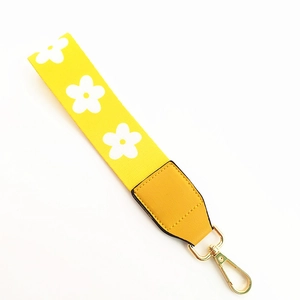 Detail of yellow floral handbag strap with golden metal clasp and leather reinforcement