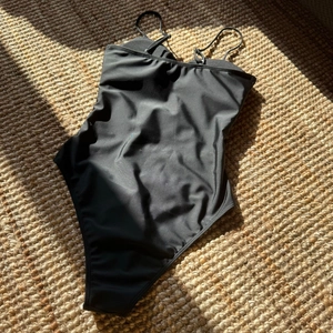 Détail d'un maillot de bain une pièce noir avec anneau métallique sur tapis tressé