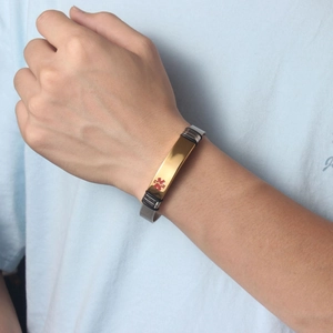Detail of medical alert ID bracelet with gold plate and red emergency symbol on wrist