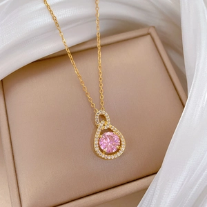 Elegant gold chain necklace with pink teardrop crystal pendant on beige jewelry tray