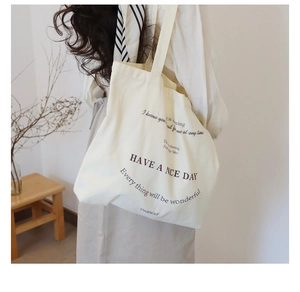 Cream canvas tote bag with 'HAVE A NICE DAY' print worn by a model in a cozy home setting