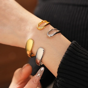 Polished gold and silver teardrop open bangles set on a model with a minimalist design