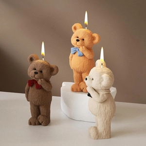 Drei handgefertigte 3D-Bärenkerzen mit bunten Schleifen auf einem minimalistischen Steinsockel