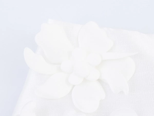 Macro shot of a white fabric floral appliqué with delicate 3D layered petals and texture