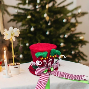 Christmas tree topper hat with festive elf legs and striped bow on blurred tree background