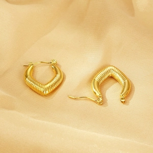 Macro detail of gold V-shaped textured earrings on champagne silk fabric background