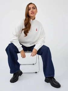 Close-up of white quarter-zip sweatshirt with red heart logo and high-collar detail