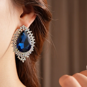 Macro shot of large blue teardrop gemstone earring with silver rhinestones on model