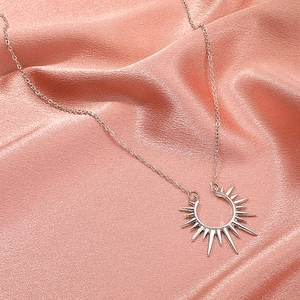 Collier vintage argenté avec pendentif soleil à pointes sur fond de satin rose chic