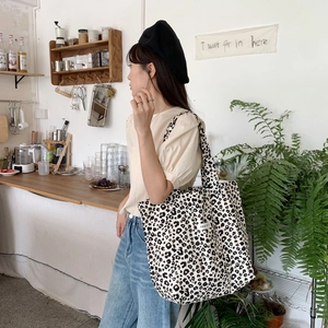 Detailed view of leopard print canvas tote bag styled on model in a cozy cafe setting