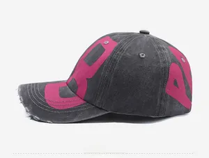 Detailed side view of washed black cotton baseball cap with pink printed letters and frayed brim