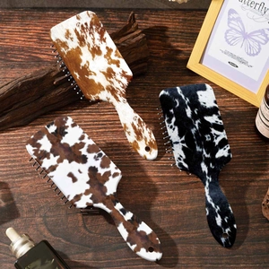 Detail shot of cow print cushion hairbrush with scalp massage and anti static functions.