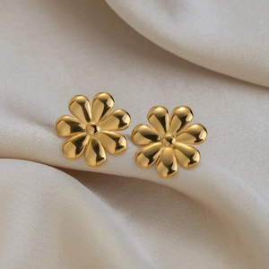 Close-up of golden 18K gold-plated flower stud earrings on soft beige silk fabric