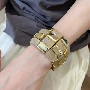 Detail view of the wide bangle featuring gold metal and off-white marbled resin links