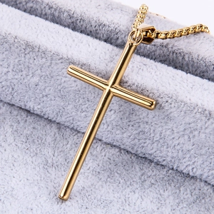 Macro shot of a golden stainless steel cross pendant on a gray velvet background