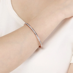 Dettaglio del bracciale rigido in oro rosa con pavé di diamanti al polso, finitura 18 carati