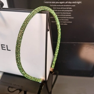 Close-up of sparkling green rhinestones on a slim headband with gold metal ends
