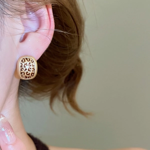 Close-up of leopard print oval stud earrings with gold trim worn by a model