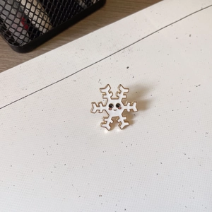 Close-up of a cute snowflake enamel pin with a cartoon face and golden metal edges