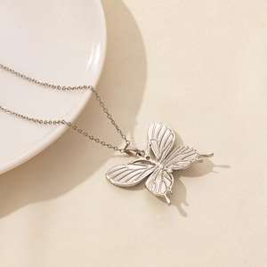 Close-up of a silver butterfly pendant necklace with intricate hollow texture on a ceramic plate