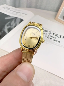 Close-up of a vintage gold oval quartz watch with a woven mesh strap and Roman numerals
