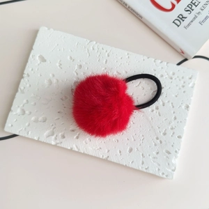 Detailed view of plush red faux fur ball hair tie with elastic black rubber band