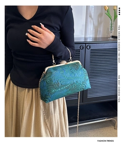 Close-up of green peacock feather textured handbag with golden metal frame clasp and chain