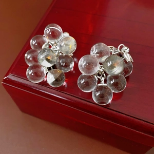 Close-up of crystal grape tassel earrings with silver needles on a vintage wooden box