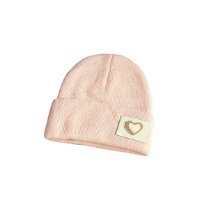 Detailed view of pink knitted beanie with heart label and high-quality stitch texture